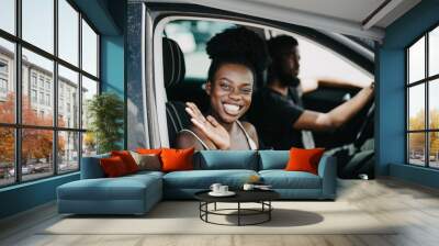 Smiling african couple in car with coffee. Young african girl looking at camera and greeting someone while drink coffee. African man at the wheel drive car Wall mural